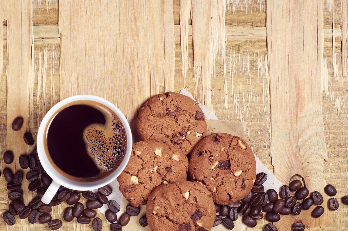 Chocolate cookies with nuts and cup of hot coffee on old wooden table, top view